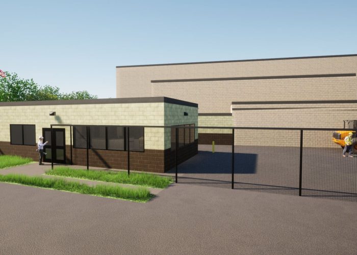 Manufacturing facility exterior with security fence and equipment in yard.