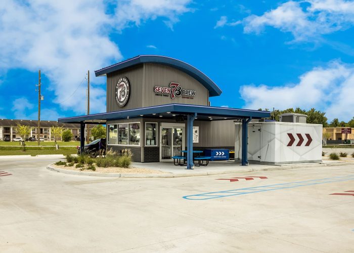 Drive-thru coffee kiosk with Seven Brew branding against a clear blue sky.