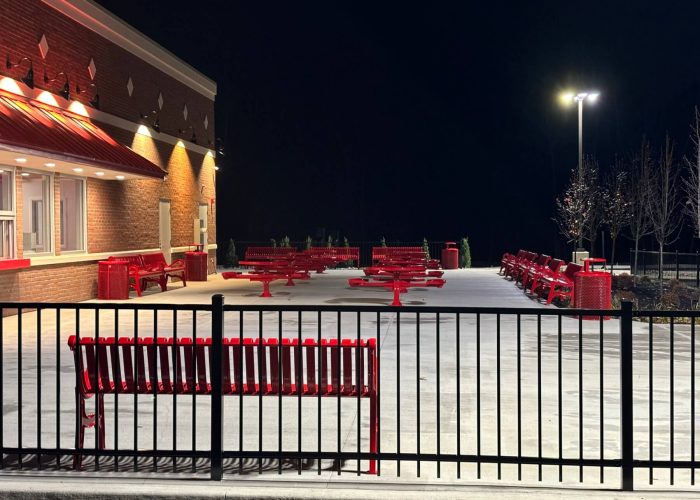 Outdoor seating area with red benches and tables at night outside a brick building.