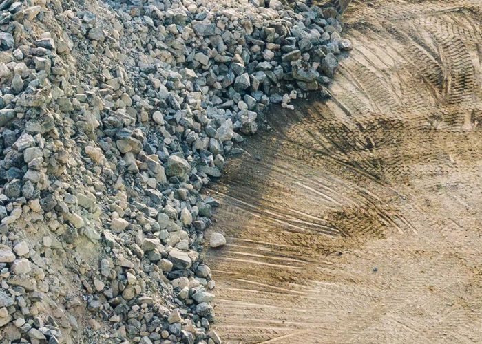 Piles of gravel at a construction site with visible tire tracks in soil, showcasing raw materials.