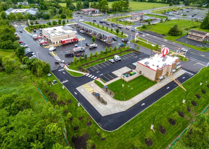 Aerial view of a busy gas station and convenience store surrounded by green landscape, showcasing parking and service areas.