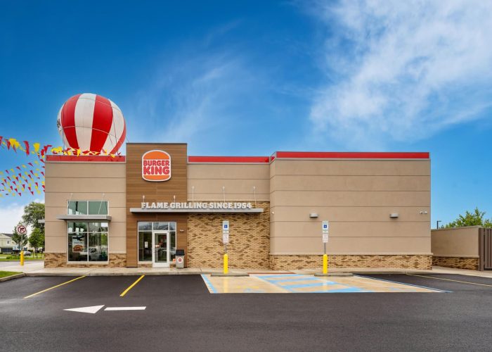 Burger King restaurant exterior with blue sky. Accessible parking and bold signage highlight flame-grilling tradition.