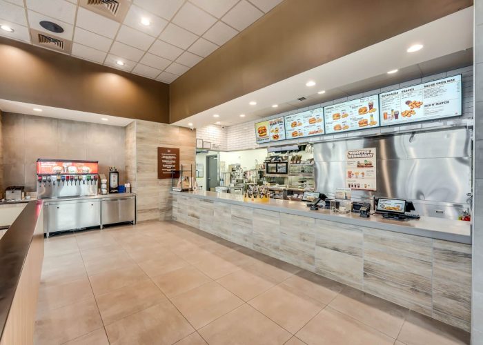 Modern fast food restaurant counter with menu boards and soda fountain, offering a variety of quick meal options.