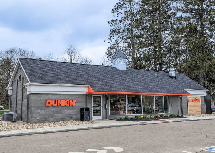 Dunkin' storefront with coffee signage set amidst trees and a cloudy sky, highlighting brand's cozy atmosphere.