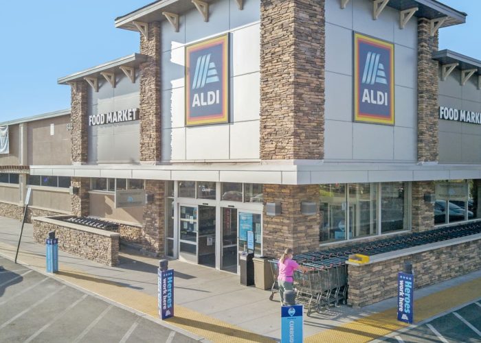Exterior of Aldi food market with shopping carts and customer at entrance, highlighting grocery store accessibility.