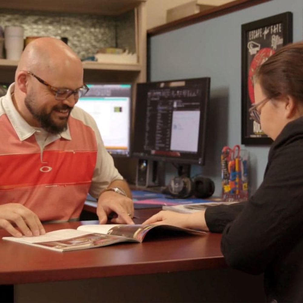 Two colleagues discuss a project at a desk in a creative office, enhancing collaboration.
