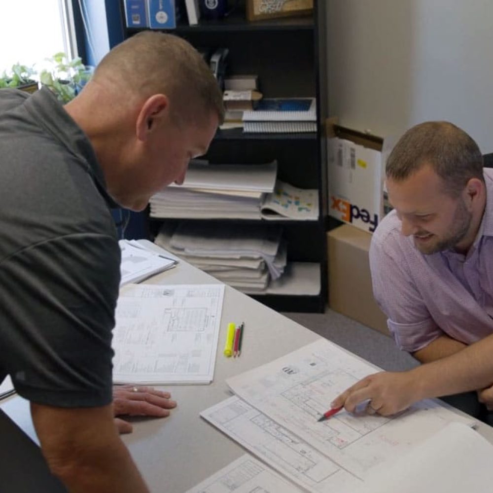 Two colleagues reviewing architectural blueprints at an office desk, discussing design plans.