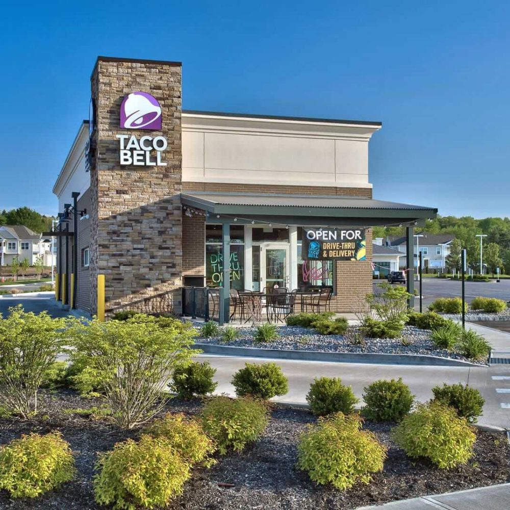 Taco Bell exterior with drive-thru and delivery signs on a sunny day.