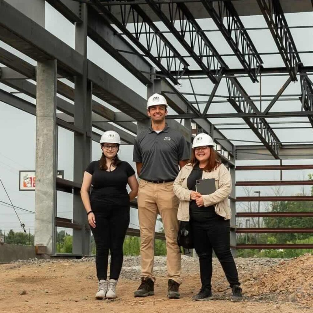 Construction team at a building site under steel framework, wearing hard hats.