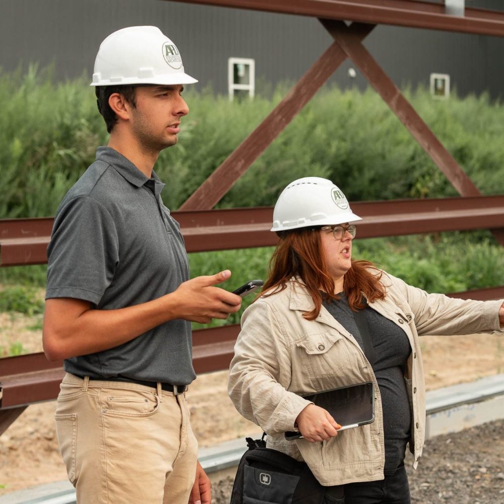 Construction workers in hard hats discuss project site logistics outdoors.