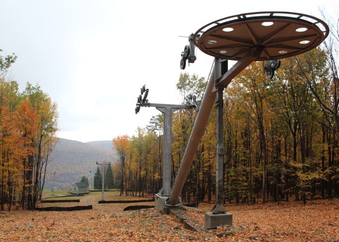 Old ski lift in an autumn forest with orange leaves and mountain views, perfect for fall hiking adventures.