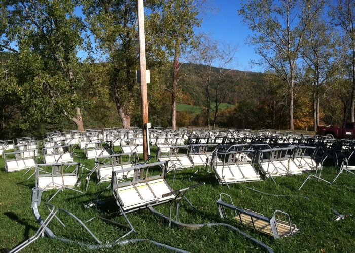 Ski lift chairs rest on grassy hillside during off-season, awaiting repair.