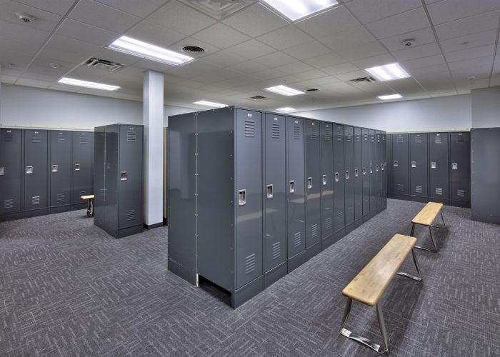 Modern gym locker room with gray lockers and wooden benches.