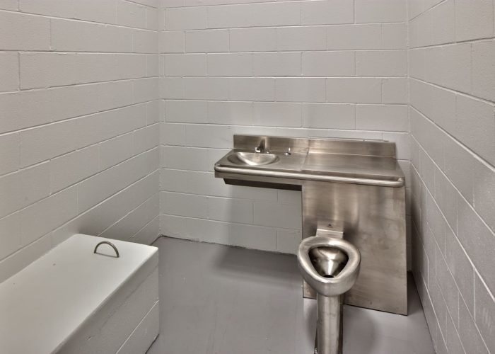 Stainless steel prison cell toilet and sink combo in a secure room setting.