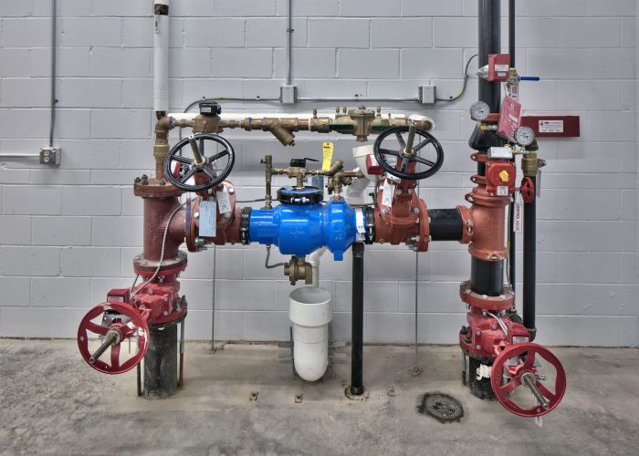 Industrial backflow prevention system with blue valve and pressure gauges in a maintenance room setting.