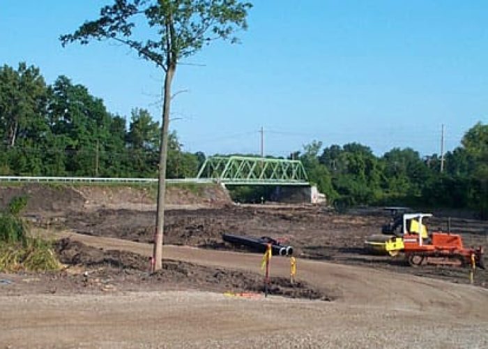 Construction site development with machinery near a bridge, emphasizing land preparation by GreenTech Construction.