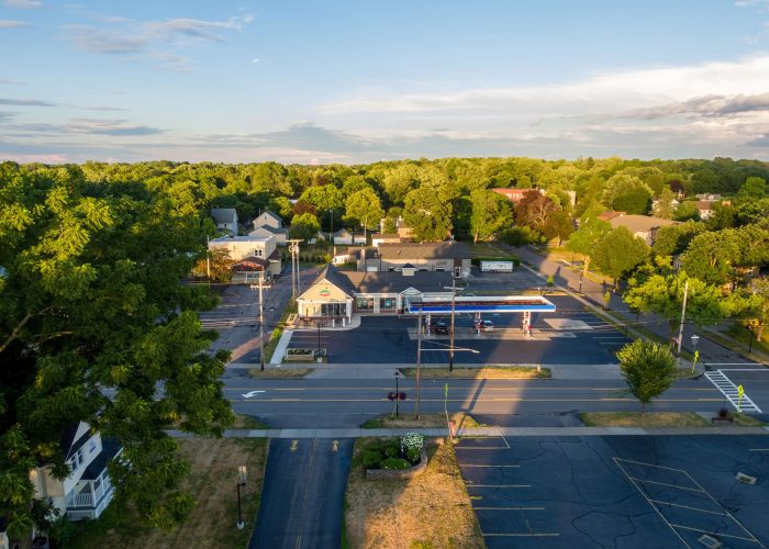 Aerial view of a gas station surrounded by lush greenery on a sunny day, capturing a peaceful small-town scene.