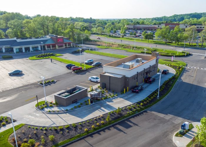 Aerial view of coffee shop drive-thru and parking lot, surrounded by greenery and shops, illustrating suburban convenience.
