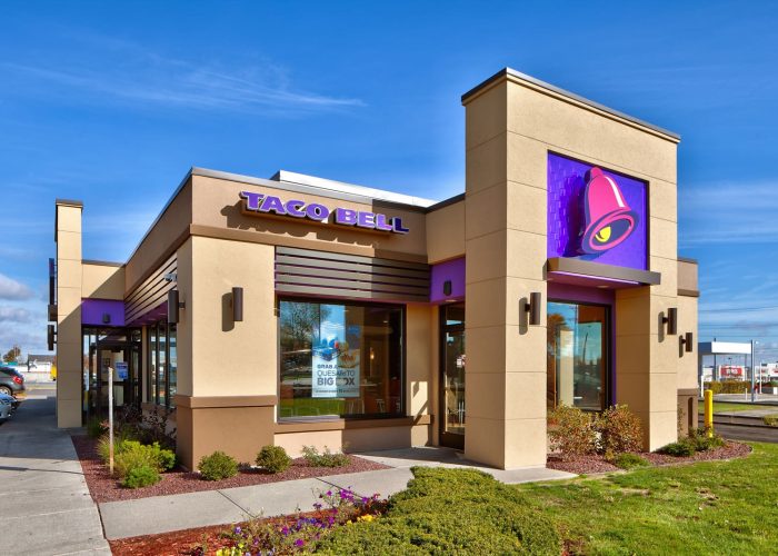 Taco Bell restaurant exterior under a clear blue sky, highlighting brand signage and architecture.