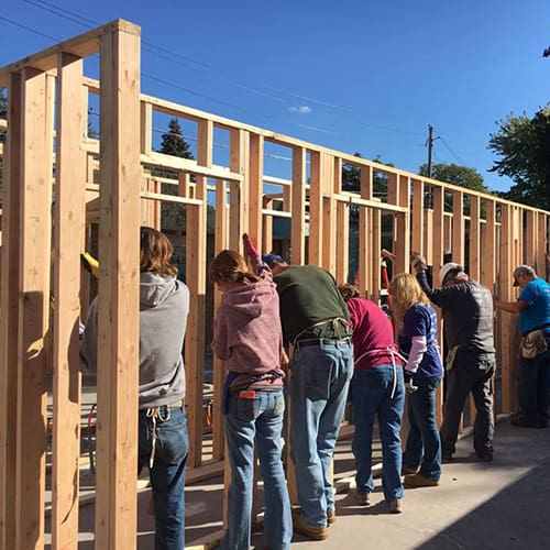 Volunteers constructing a wooden frame in a community building project under a clear blue sky.
